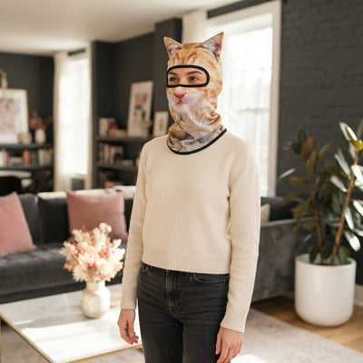 A smiling woman wearing a 3D cat face balaclava mask, captured in a bright, modern room with rose and charcoal decor.