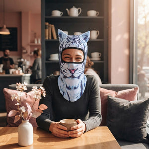 A person wearing a realistic cat face balaclava mask, smiling in a modern cafe with soft rose and charcoal decor.